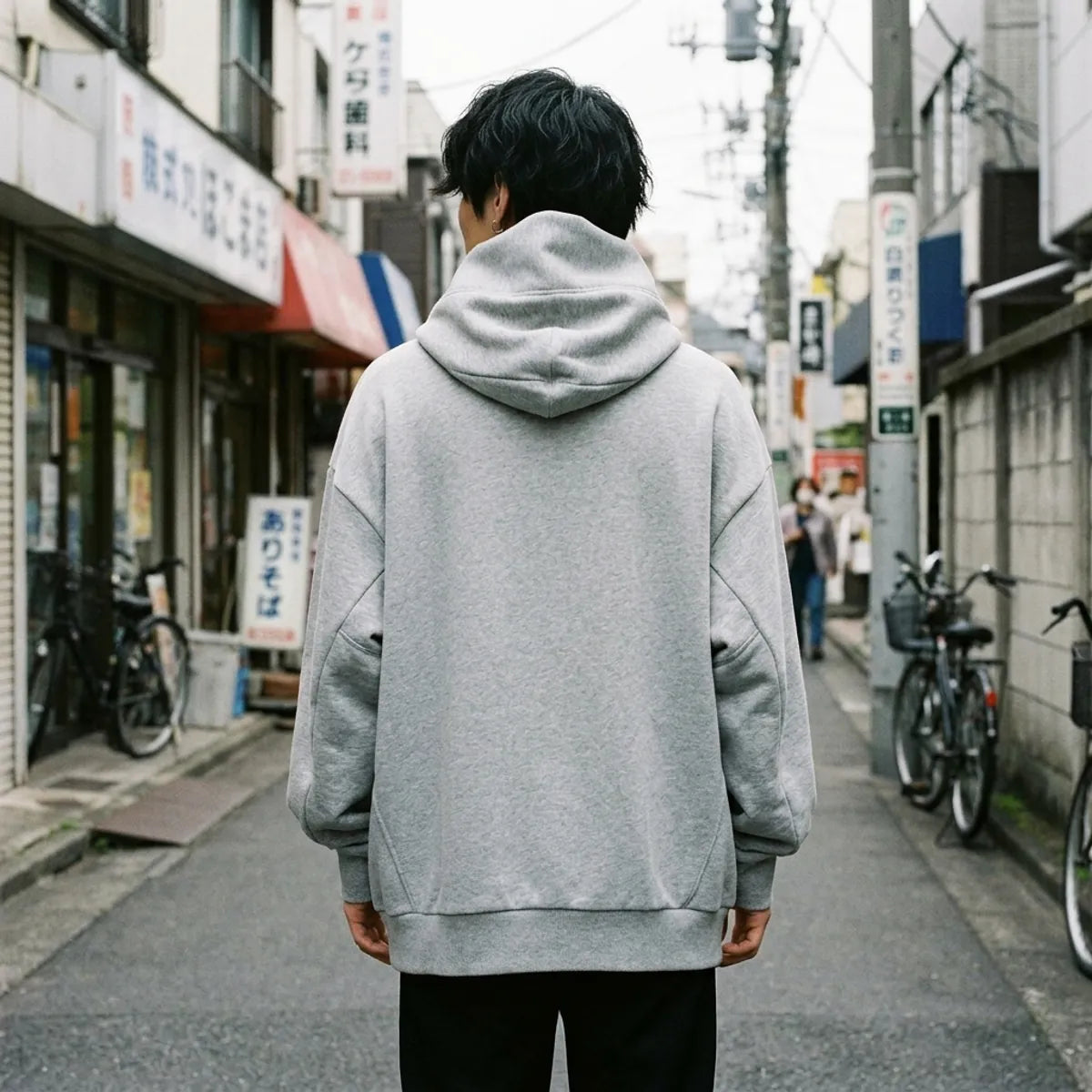 The back of the grey oversized hoodie, plain heather grey with the tall funnel hood rising behind the head