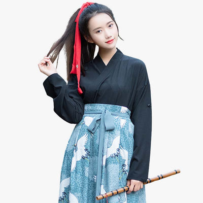 A woman is wearing a Hakama skirt with a Japanese Tsuru (crane) motif printed on the fabric. She is holding her hair and wearing a black kimono top.
