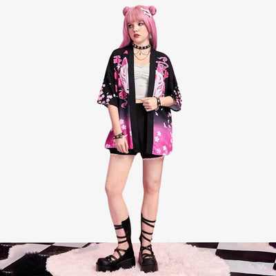 A woman is dressed with black Haori kimono for women, inspired by traditional pattern as the white kitsune fox mask and the japanese blossom flowers (sakura). The haori jacket is crafted with a kawaii style outfit