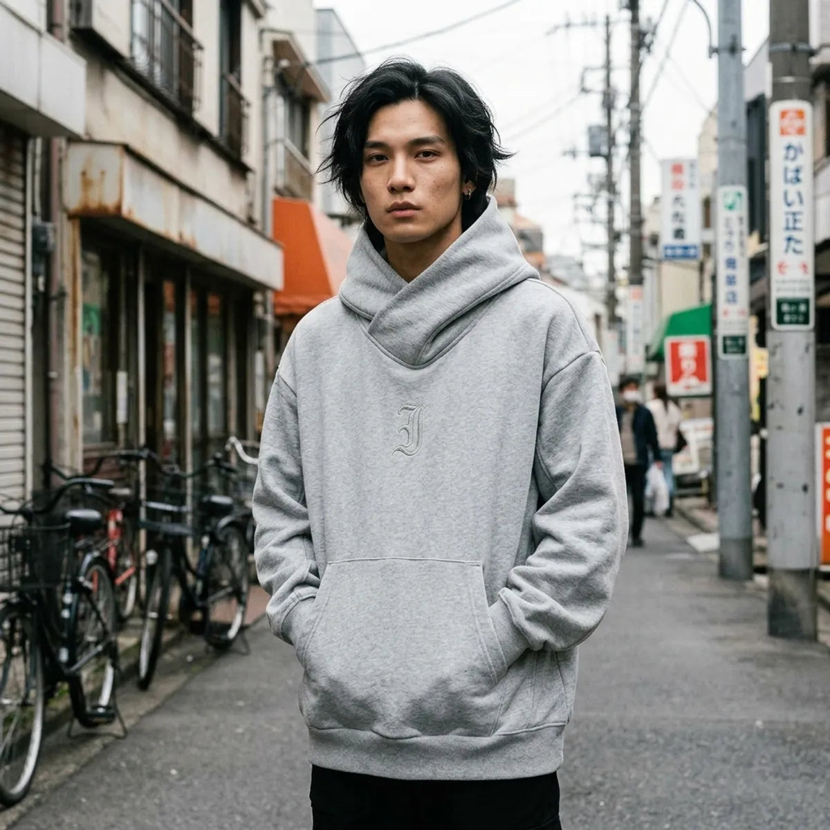 Grey Harajuku hoodie with a crossed chimney collar, worn oversized with hands in the kangaroo pocket in Harajuku