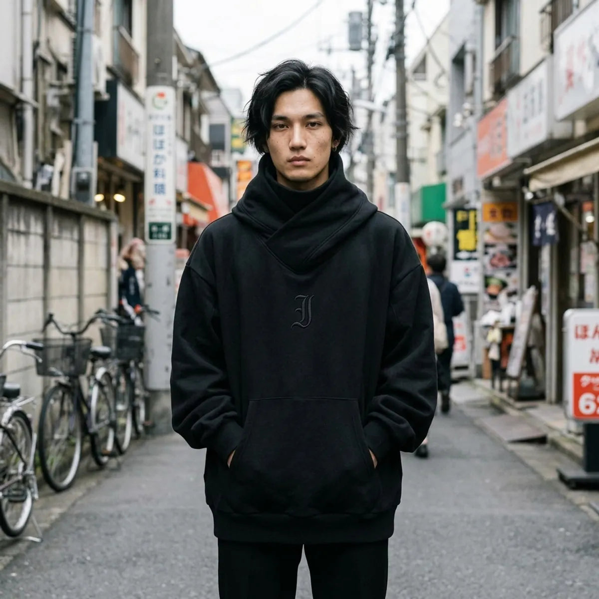 Black Harajuku style hoodie with a crossed chimney collar, worn oversized with hands in the kangaroo pocket