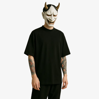 a man is dressed with a full black japanese harajuku shirt. His face is hided with a white hannya mask. He has irezumi tattoo on harms. Tje japanese t-shirt s oversize