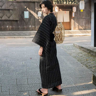 A teenager from the back is wearing a japanese-black-kimono-cosplay. He is wearing Japanese Geta sandals on his feet.