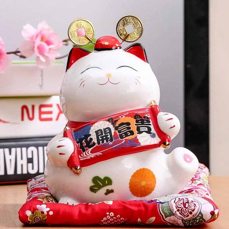 This Japanese cat box piggy bank is a ceramic maneki neko cat. This decorative object brings good luck. The white cat is in ceramic and is holding a Makimono ribbon in its paws.