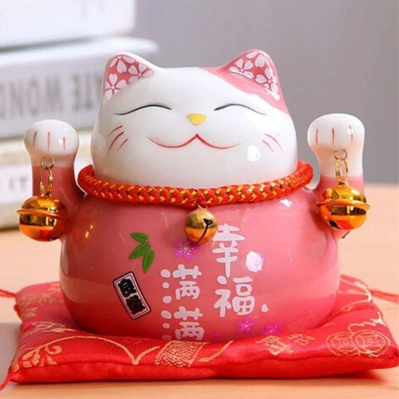 A japanese cat piggy bank on a red cushion. The Japanese cat statuette is holding bells. This Japanese decorative object is made of ceramic and hand-painted with acrylic paint.