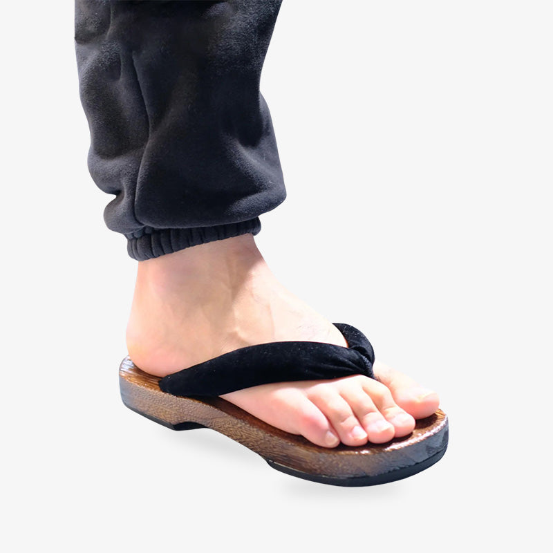 Simple yet stylish Japanese flip flops, ideal for everyday comfort. The man is wearing the japanese zori sandals on his right feet. The materal used is wood, and silk black strap