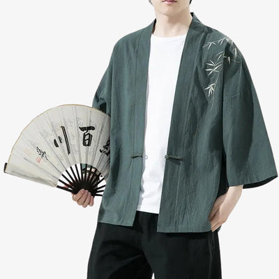 Person wearing a green japanese haori kimono cardigan style with bamboo embroidery, holding a fan with Japanese Kanji black text.