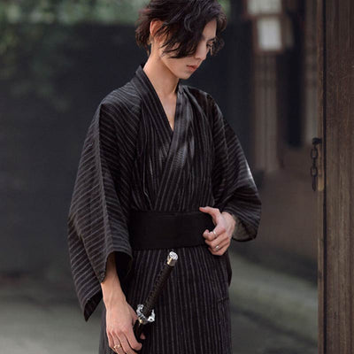 Put on a Japanese kimono for men for traditional samurai style. The man is holding a black obi belt and a katana.