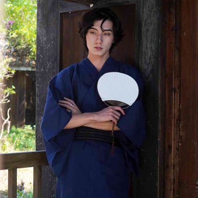 A man is wearing a traditional Japanese kimono robe men. He hold a white japanese sensu fan in his left hand.