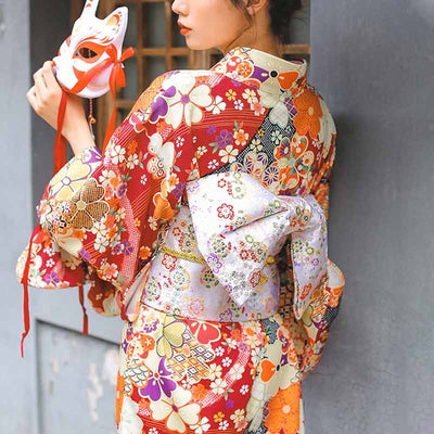 A geisha is dresse with a japanese kimono yukata kaku obi belt. The kimono fabric is printed with sakura patterns. The japanese kimono for women is red