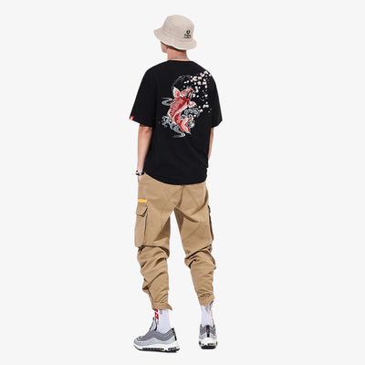 Person wearing a black Japanese Koi t-shirt with a Japanese fish design, beige pants, and a beige bucket hat on a white background