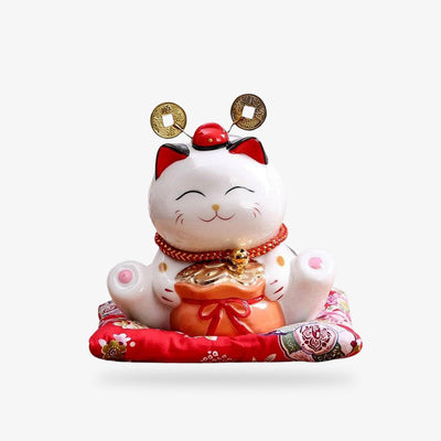 This japanese lcky cat maneki neko is white colored. It is in ceramic on a red cushion. It has a bag full of gold coins.