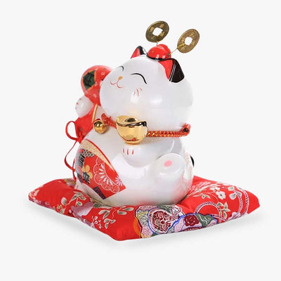 The Japanese maneki neko lucky fortune is made of ceramic. The colour of the Japanese lucky cat is white and red. It is a lucky cat resting on a red cushion.
