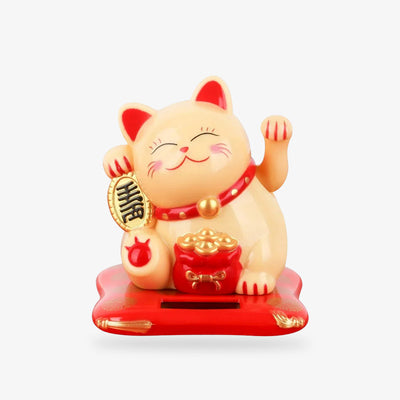 This Japanese Maneki Neko cat is yellow and golden. This lucky Japanese cat is holding a golden koban in its right paw. His left paw is raised. There is a bag of gold coins in front of him. He has a red collar with a bell around his neck and the inside of his ears is also red.