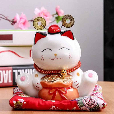 The japanese maneki neko lucky cat is a ceramic cat peggy bank. Material is ceramic. Maneki Neko money box on a red cushion.