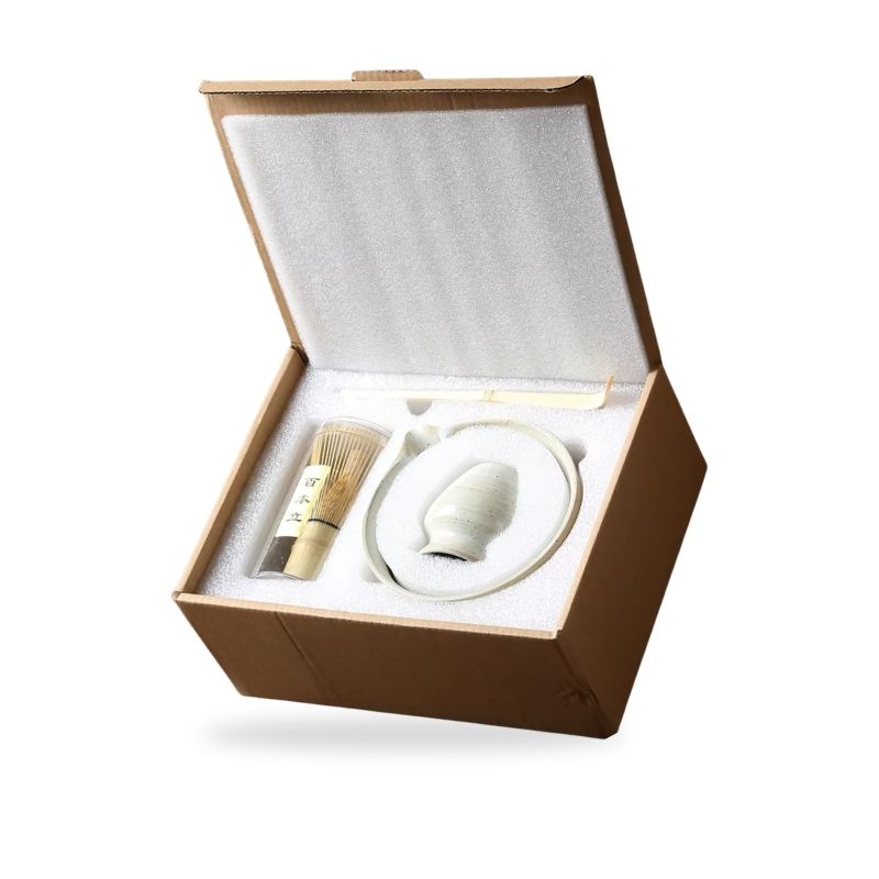 Open brown Japanese matcha gift box containing a white ceramic item and a brush on a white background