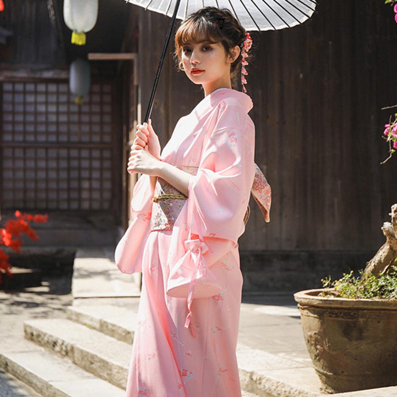 A woman is wearing a traditional Japanese obi saura kimono and an Obi geisha belt around her waist. She holds a Japanese parasol in her hand. The geisha has a Kanzashi in her hair.