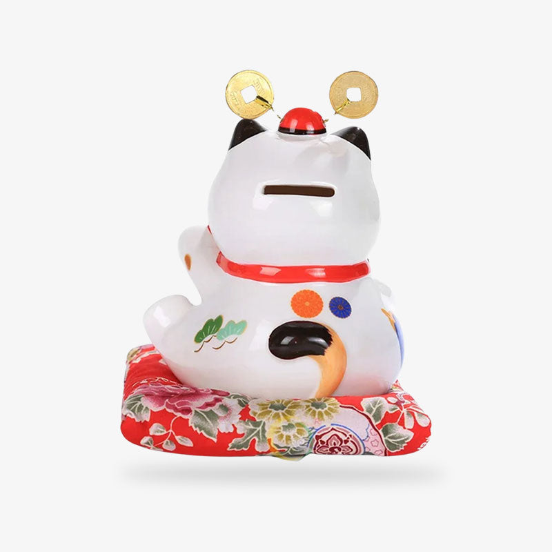 This Japanese piggy bank cat in box has a slit at the head. It is a maneki neko money box placed on a red cushion.