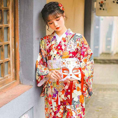 apanese red kimono robe with printed sakura flower designs. The woman is holding a Kitsune mask in her hand