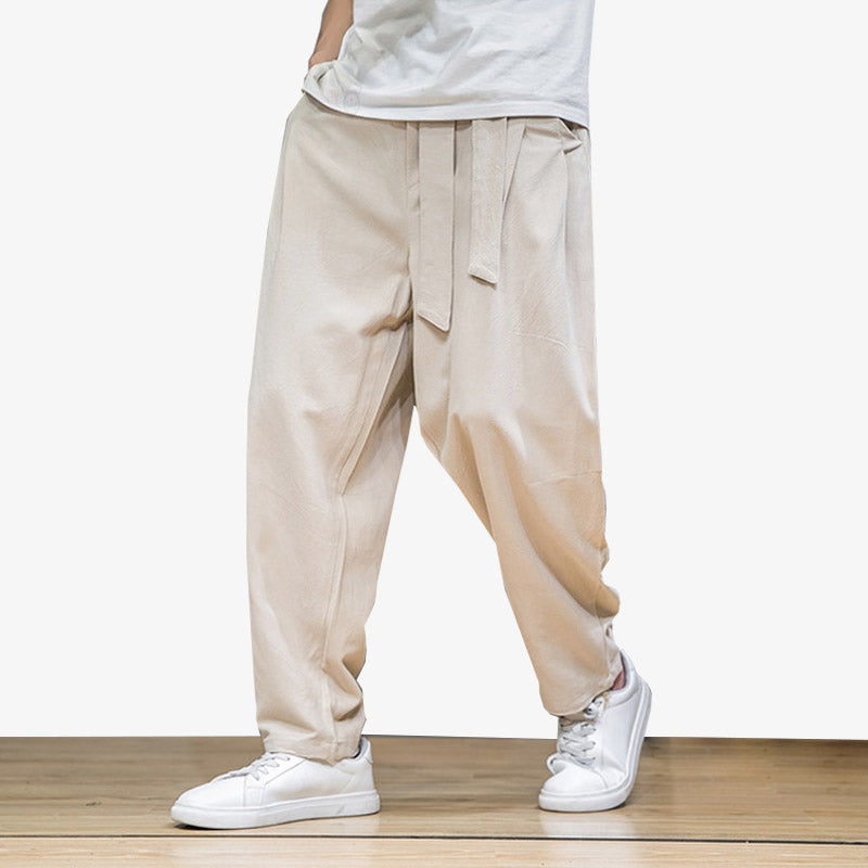 A man is wearing beige Japanese-style pants. On his feet are a pair of white sneakers. The japanese pants are wide with a belt.
