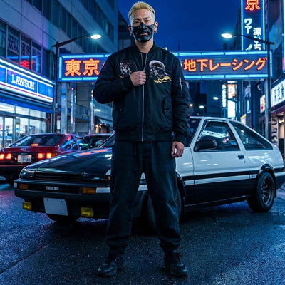 Man in a black Japanese Sukajan jacket standing in front of a classic car on a neon-lit Harajuku street at night.