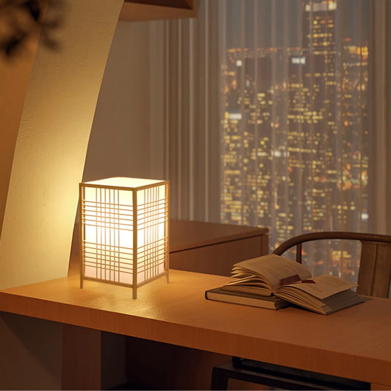 Japnese Table lamp on a desk with books and a cityscape view through a window.