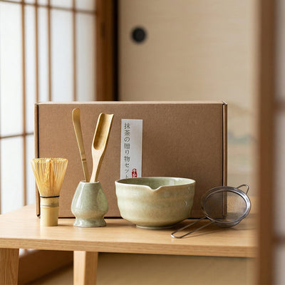 Tea-making set with a bowl, whisk, and other tools on a wooden table.