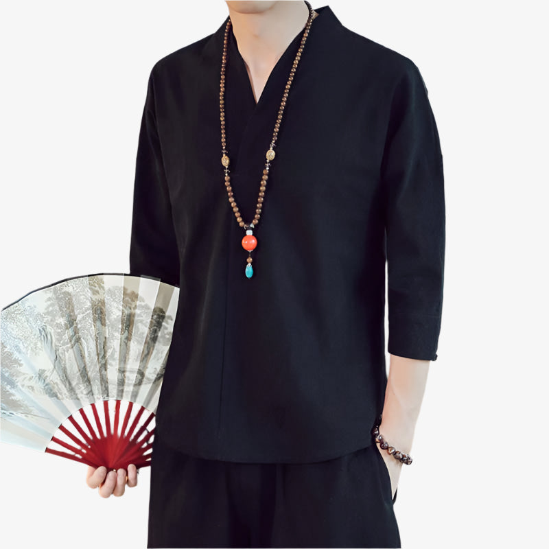 A man dressed with black japanese tshirt and holding a fan. He wear a buddhist necklace