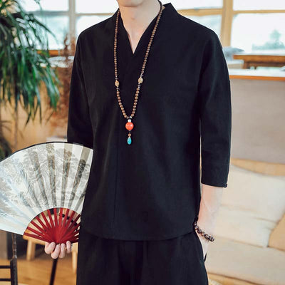 A man dressed with black japanese tshirt and holding a fan. He wear a buddhist necklace