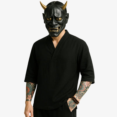 Person wearing a black Japanese demon mask and japanese v-neck shirt with Irezumi tattoos visible on arms.