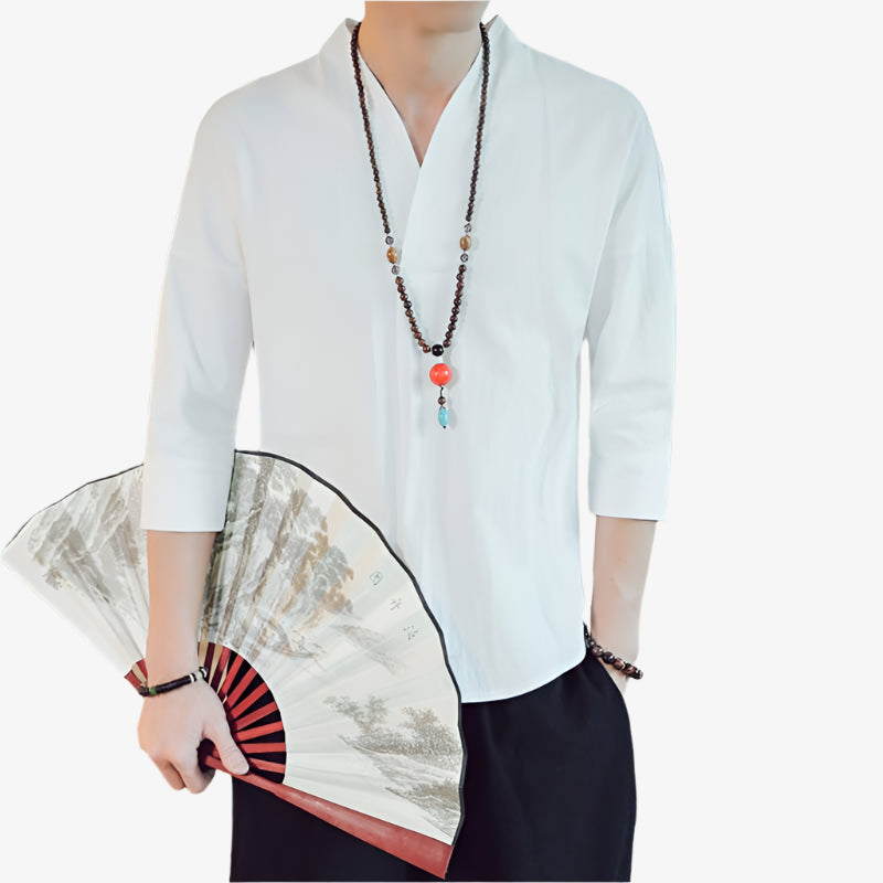 A man is holding a fan in his hands and he is dressed with a japanese white shirt taditionall