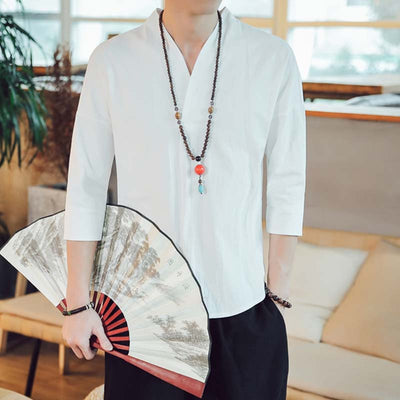 A man is holding a fan in his hands and he is dressed with a japanese white shirt taditionall