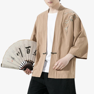 Person wearing a beige Kimono Haori Jacket floral pattern with embroidery, holding a fan with calligraphy, on a white background