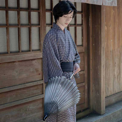 A Japanese man is wearing a kimono motif sasa suisen seigaiha. Kimono material is cotton. Japanese wave motif is printed on the Yukata fabric. The traditional garment is fastened with an Obi belt. The man is holding a Japanese parasol.