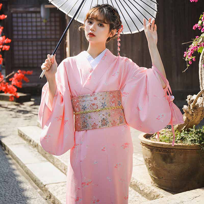 A woman is dressed in a Japanese kimono obi sakura tied with a geisha sash with floral motifs embroidered on the fabric. The Japanese woman holds a parasol in her hand.
