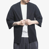 A man is wearing a white T-shirt and a long black kimono cardigan. The material is cotton and linen. This is a style of Japanese menswear worn over a kimono or yukata.