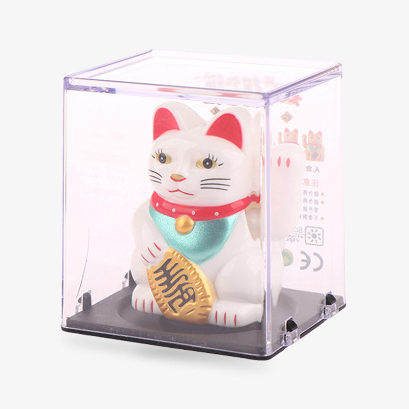 The lucky cat maneki nejo is packaged in a square plastic box. The lucky cat is white with red ears inside. It has a red collar and holds a Koban coin in its paw. His second left paw attracts luck and good fortune.