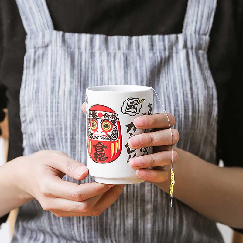 The made in Japan tea cups are adorned with a striking red Daruma motifs and black kanji symbols