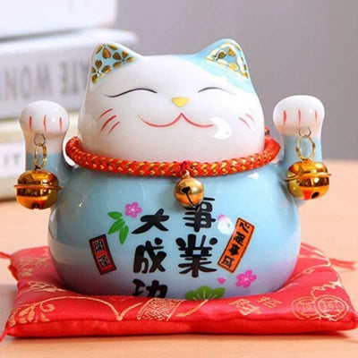 This maneki neko blue cat is in ceramic. This Japanese cat statuette is resting on a red cushion.