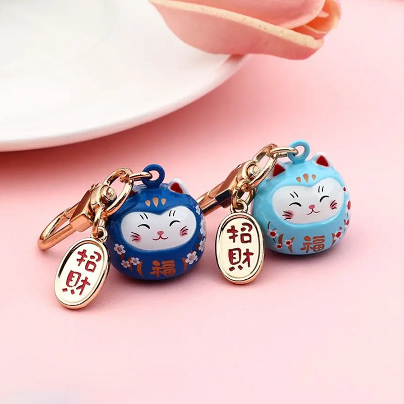 This maneki neko cat keychain is shaped like a Japanese cat. The two maneki neko cats are decorated with paintings of sakura flowers and kanji. The brass metal part of this Japanese accessory is engraved with a kani meaning good fortune.