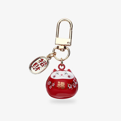 Red kawaii maneki neko keychain in the shape of a Japanese cat. The object is painted with sakura flower symbols and a golden kanji. The coin is engraved with a kani meaning "invitation to wealth" in Japanese.