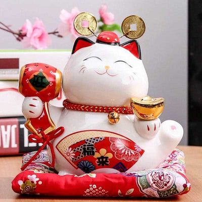 The Japanese maneki neko statue lucky cat cat is white colored. It has its right paw raised and is holding a red mallet with a kanji. Sensu fans are hand-painted. The little statuette is resting on a red cushion.