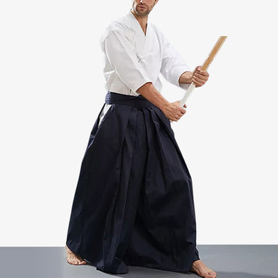 A Japanese martial artist is dressed in a blue men hakama. His equipment consists of a white keikogi and a wooden shinai katana.