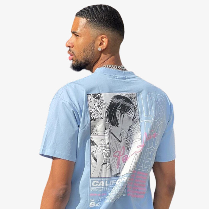 the men manga Tee is blue. The man is standing with his back to us. The Japanese T-shirt is printed with a manga design on the back.