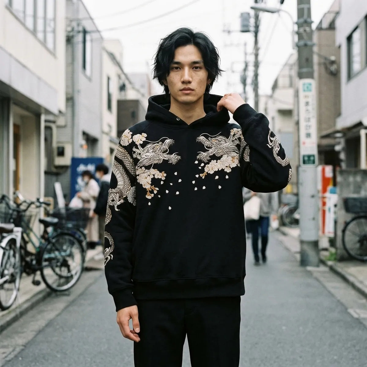Mens Japanese hoodie in black with two silver embroidered dragons on the chest, worn in a Harajuku backstreet