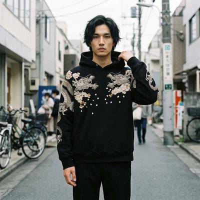 Mens Japanese hoodie in black with two silver embroidered dragons on the chest, worn in a Harajuku backstreet