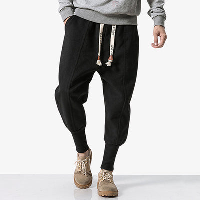 For a streetwear style, a man is dressed in black Japanese nikka pants. The bottom of the trousers is curved. The cords are printed with Japanese kanji.
