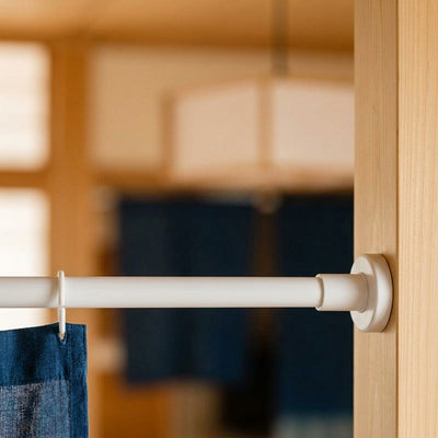 Tension rod holding an indigo noren curtain across a wooden washitsu doorway