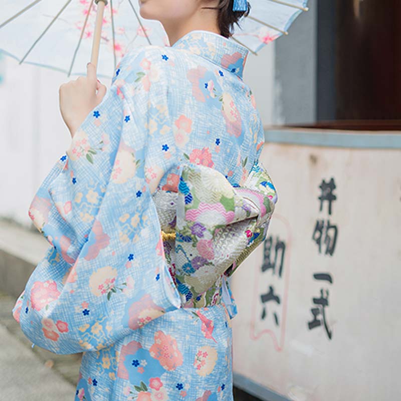 a women is standing in a Japan street. She is dressed with obi belt with floral dress. The obi knot ties the traditional kimono robe