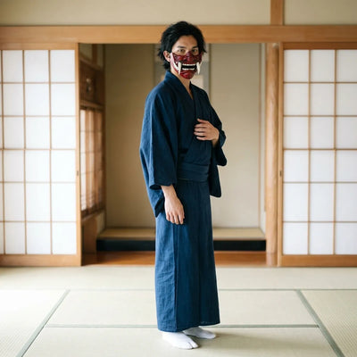 A standing model wears the maroon oni mempo mask, showing the flared wing-like side flanges and the black adjustable strap fastened along the jawline.